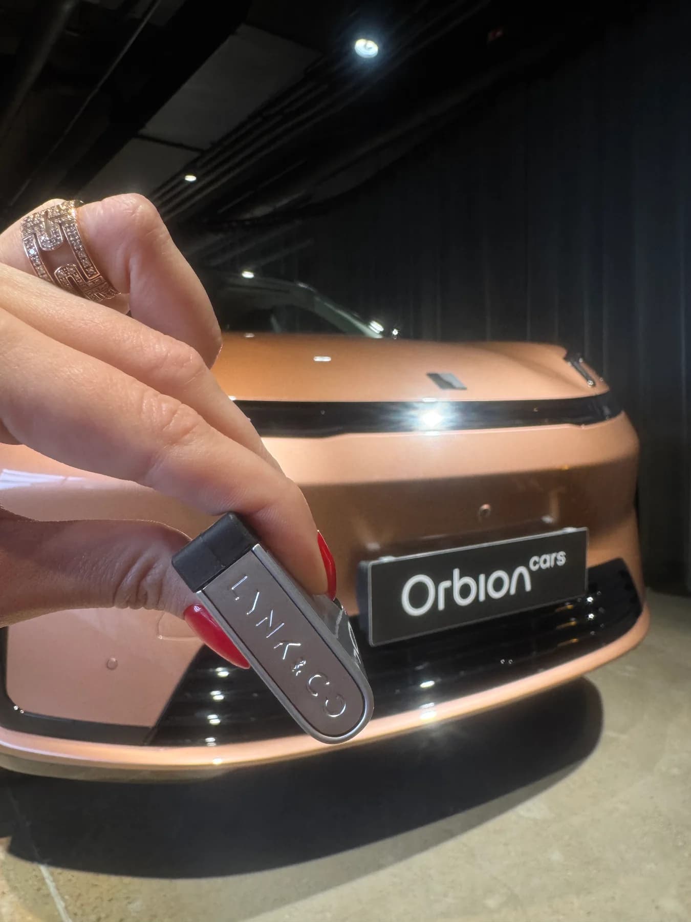 Klíč Lynk & Co před vozem s označením Orbion cars